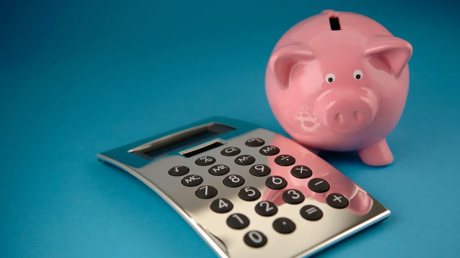 Um cofrinho de modelas de porco ao lado de uma calculadora prata